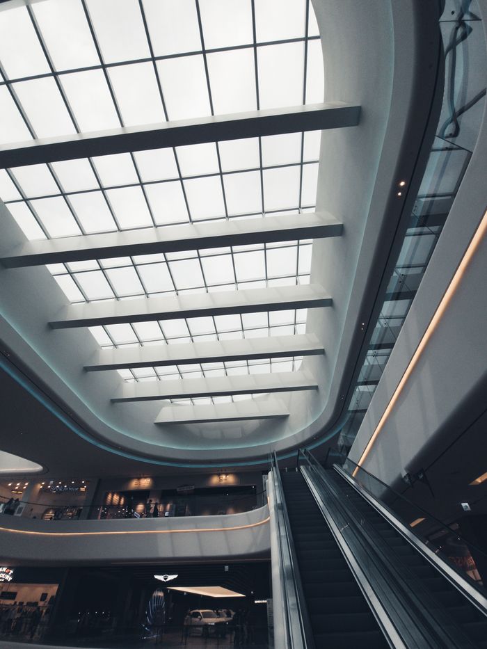 services-03 Explore this sleek interior of a modern shopping mall featuring a skylit ceiling and escalator view.