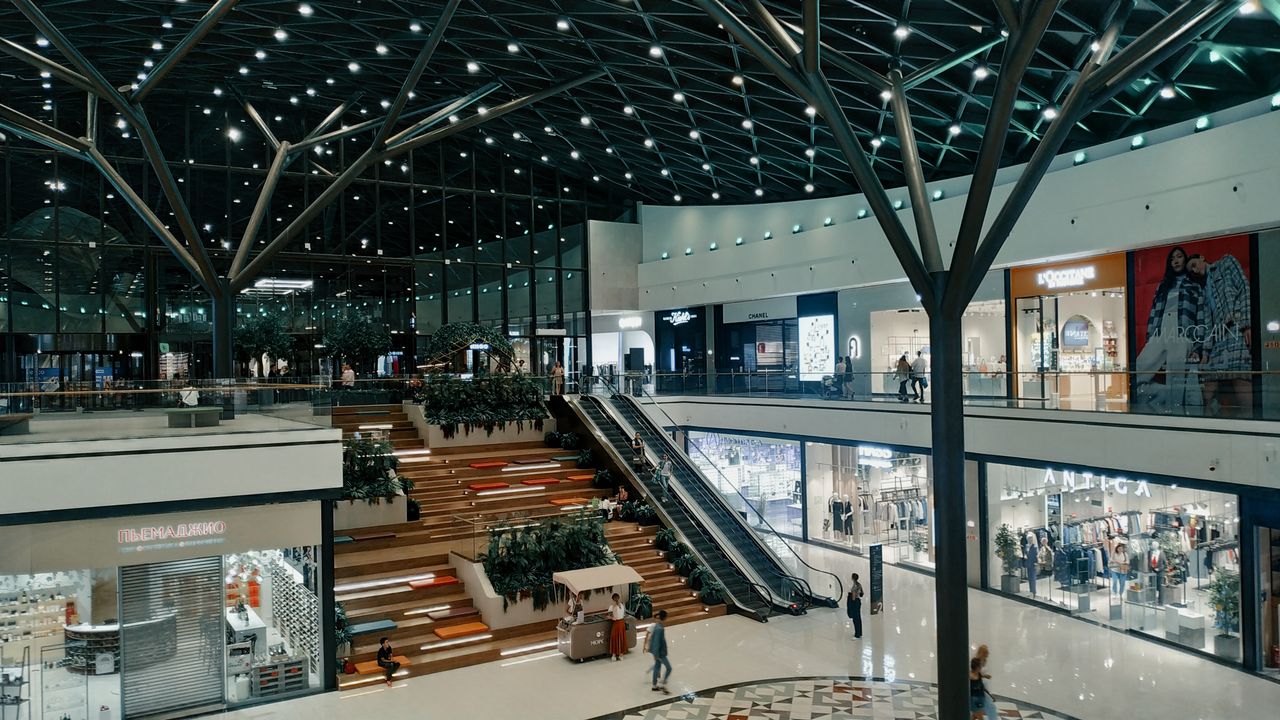 services-02 Explore a spacious and contemporary shopping mall featuring trendy shops, lush greenery, and stylish architecture.
